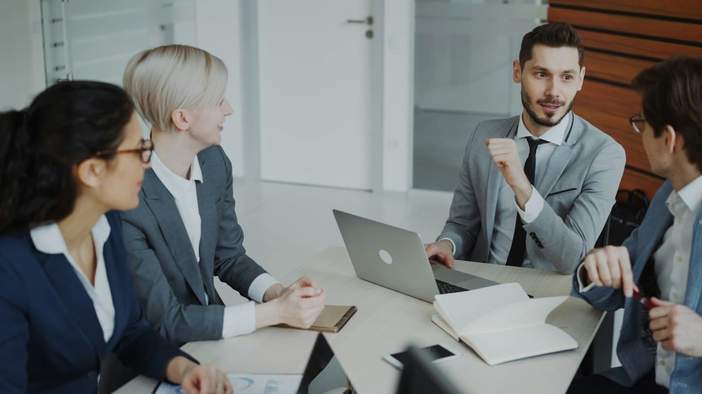 Professionnels échangeant autour d’un ordinateur et de documents lors d’une réunion.